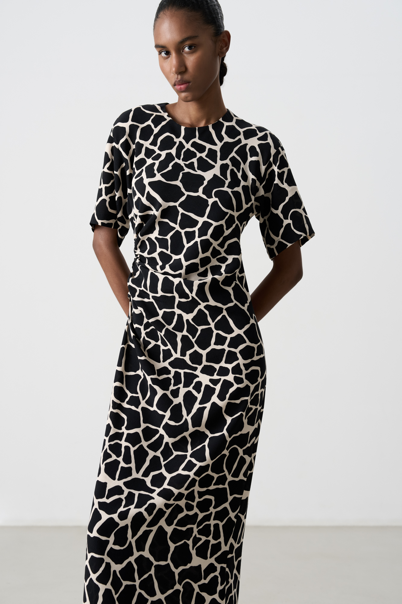 Платье длины миди из 100% вискозы с анималистичным принтом, имитирующим пятна жирафа. Модель приталенного силуэта, со спущенной линией плеча, коротким рукавом и круглым вырезом горловины. Изделие декорировано драпировкой сбоку.&nbsp;&nbsp;