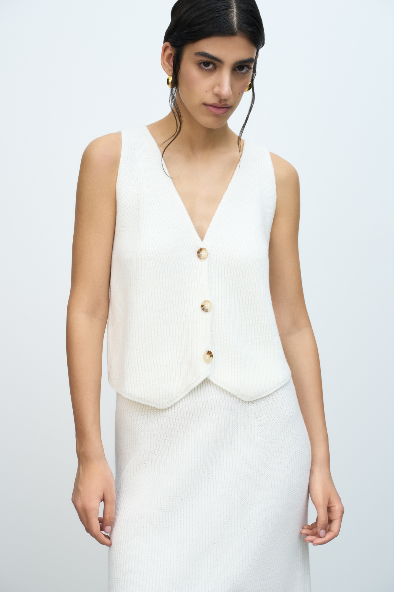 Трикотажный жилет из шерсти. Модель прямого кроя с глубоким V-образным вырезом и застежкой на пуговицы. Дополнить образ можно юбкой в таком же стиле.