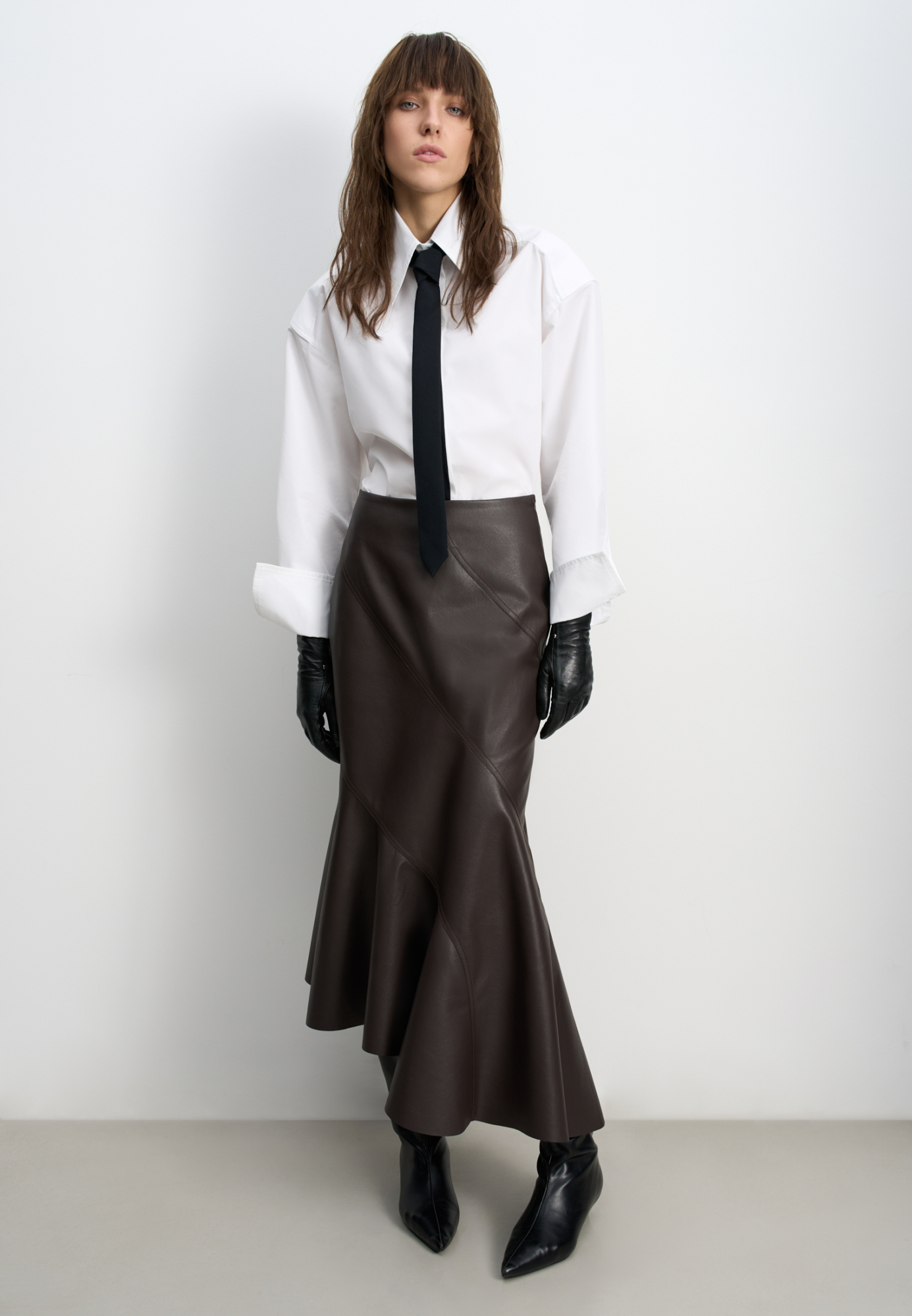 Асимметричная юбка из экокожи длины миди. Модель по фигуре с расклешенным подолом и косыми складками. Застежка на молнию сбоку.