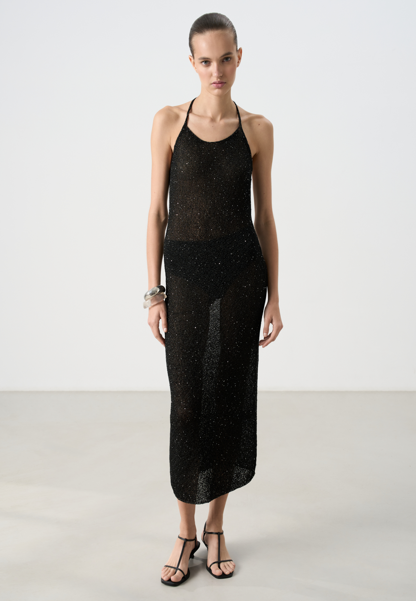 Трикотажное платье длины миди из хлопка с добавлением вискозы. Изделие декорировано мелкими пайетками. Модель прямого кроя с открытой спиной и двумя лямками-завязками на шее. Без подкладки.