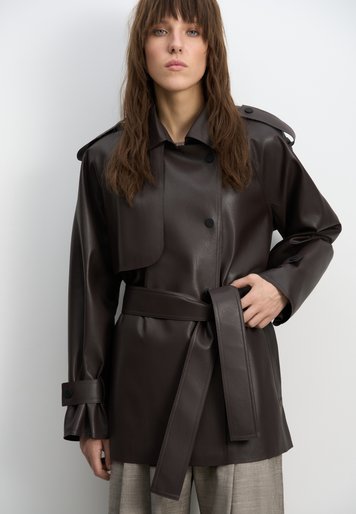 Тренч из двусторонней экокожи. Модель прямого кроя с широким отложным воротником и кокеткой. Изделие декорировано патами на плечах и манжетах рукавов. Два боковых кармана. Застежка на кнопки. 