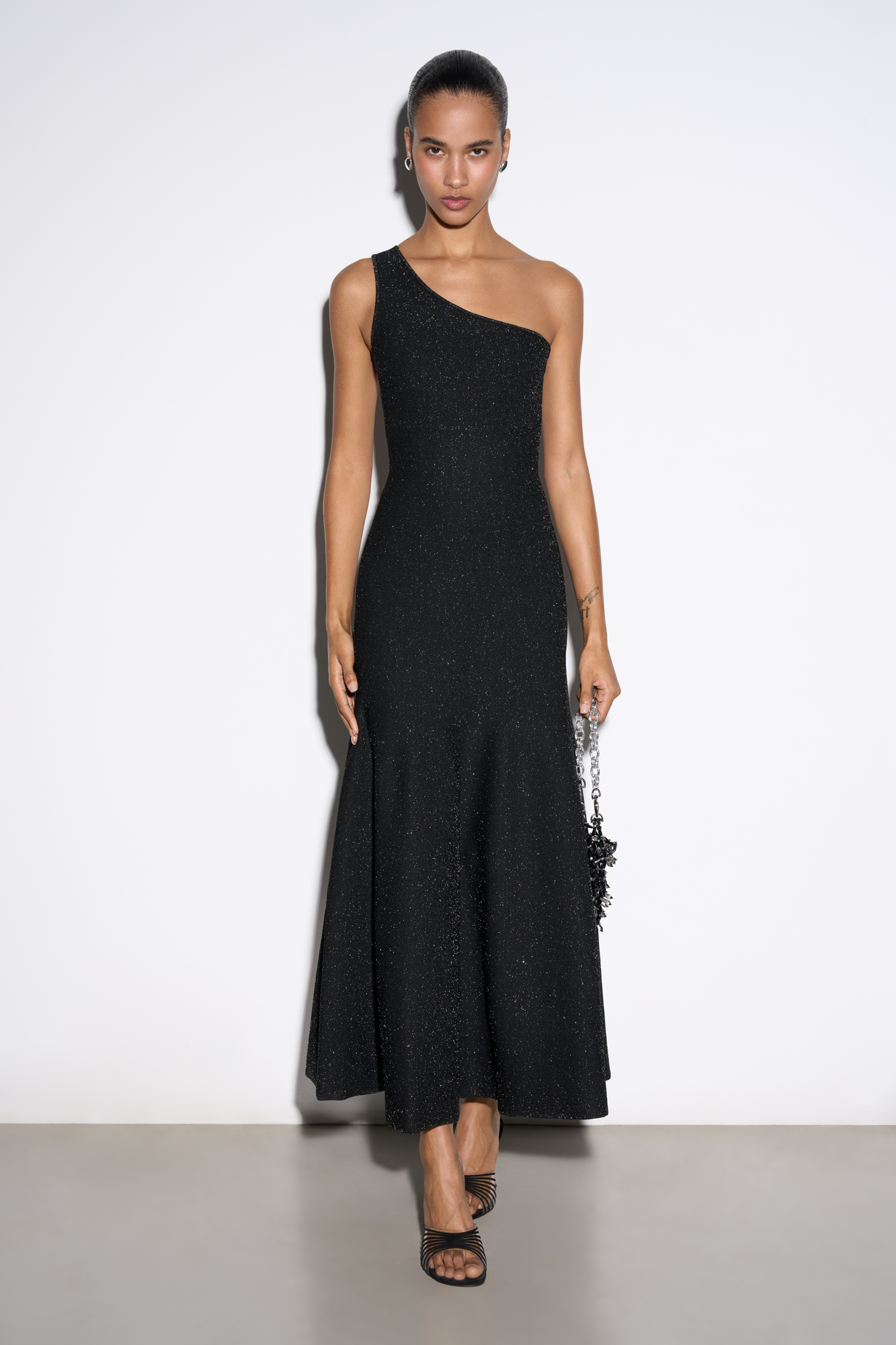 Трикотажное платье длины миди из вискозы с добавлением люрекса. Модель приталенного силуэта с юбкой, расклешенной от талии, без рукавов, с асимметричным вырезом на одно плечо.