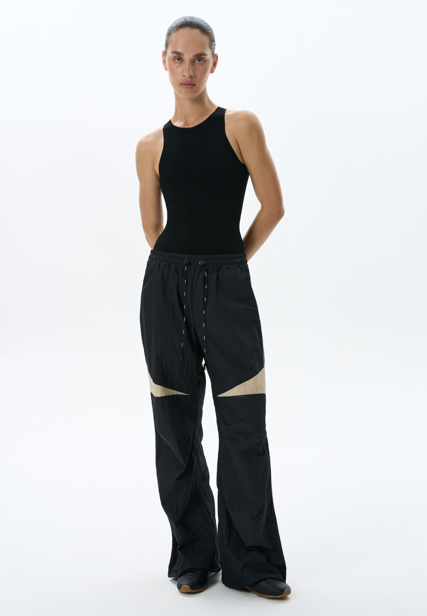 Спортивные брюки из 100% нейлона. Модель свободного силуэта, с широким эластичным поясом на резинке, дополненным кулиской. Изделие декорировано контрастными вставками. Дополнить образ можно олимпийкой в таком же стиле.