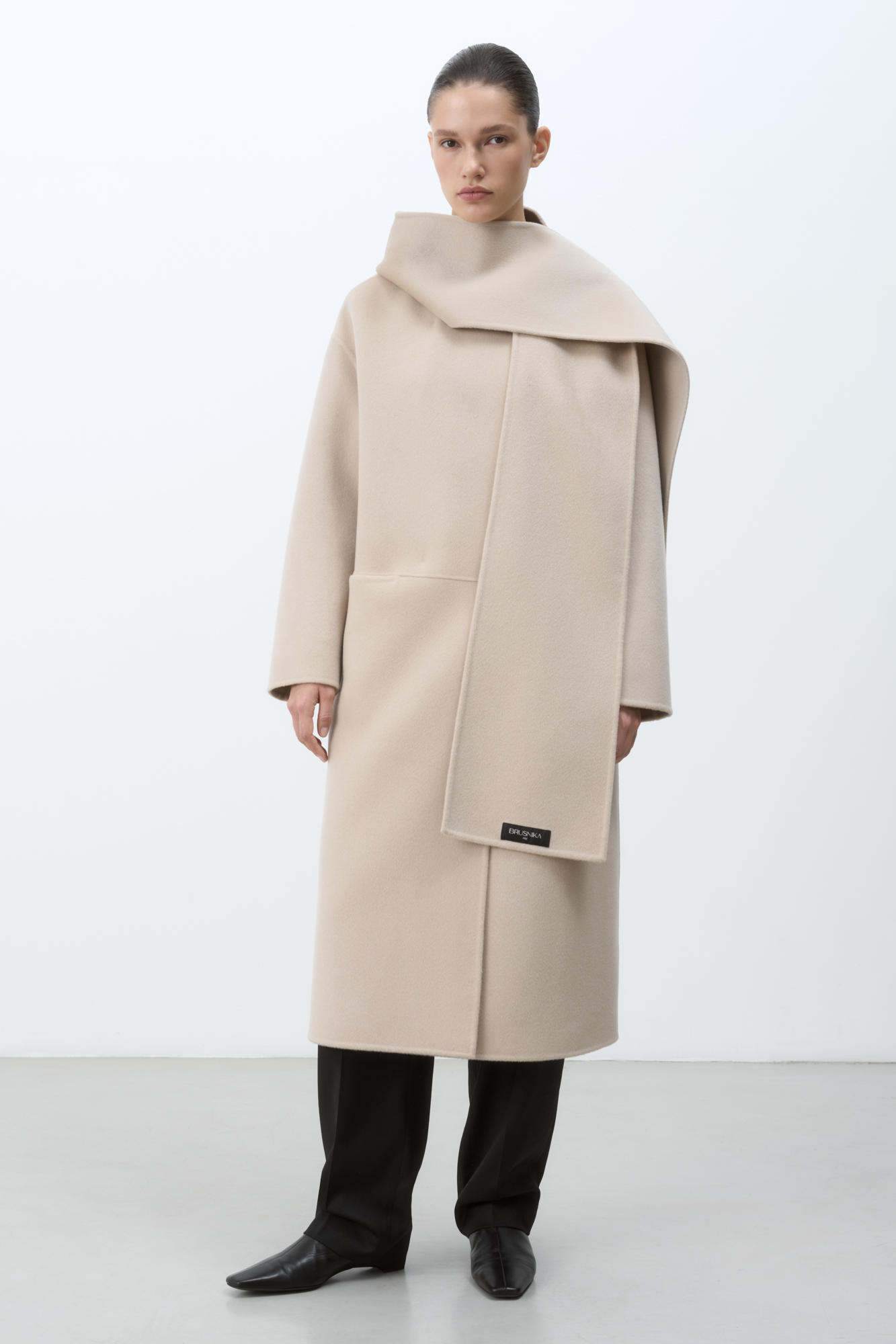 Пальто из мягкой шерстяной ткани. Модель свободного силуэта с прорезными карманами. Капюшон переходит в воротник и шарф. Брендированный ярлык на шарфе. 