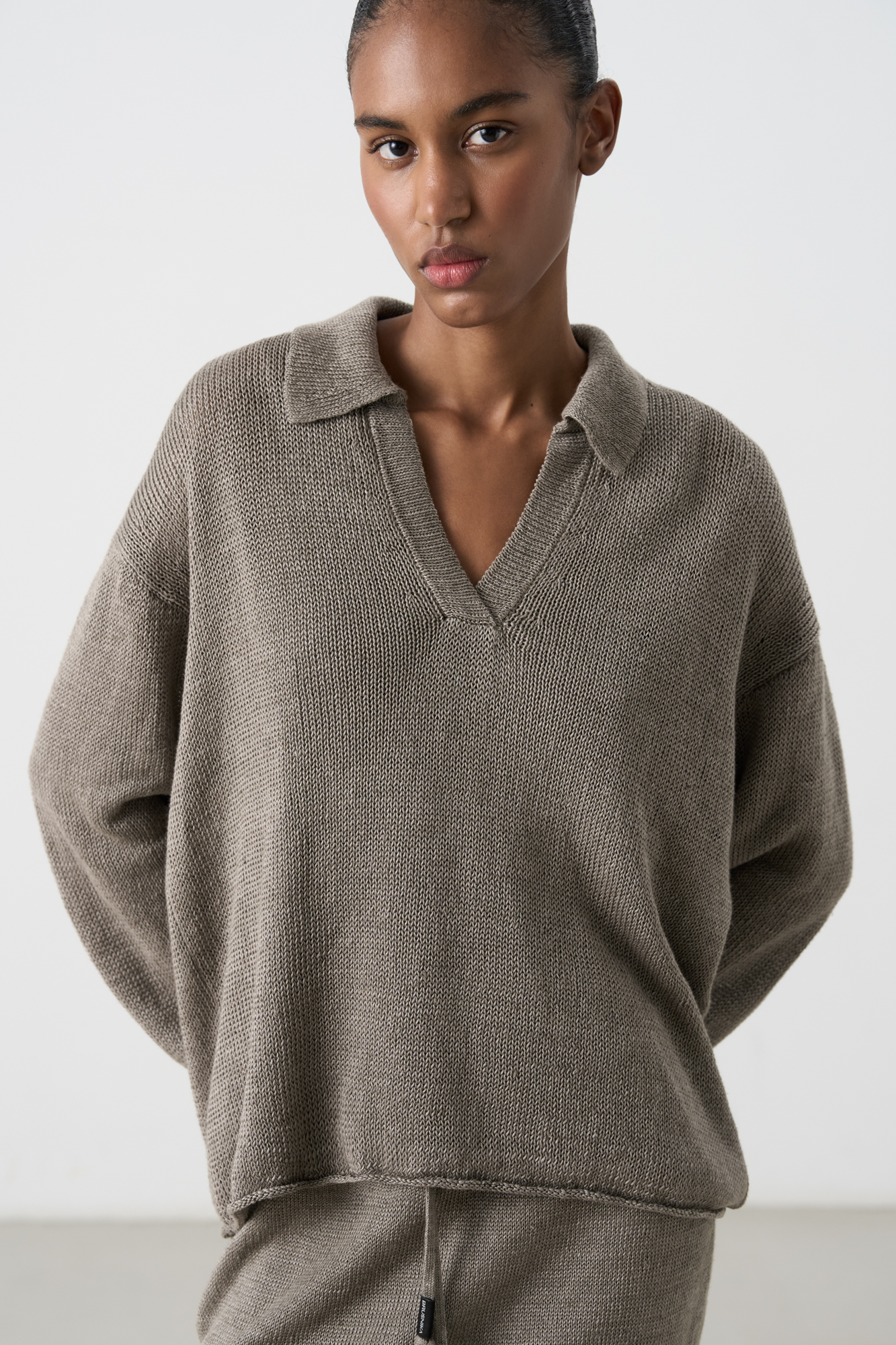 Трикотажный джемпер из 100% льна с воротником поло. Модель свободного силуэта, со спущенной линией плеча, длинными рукавами, V-образным вырезом горловины и валиками по нижнему краю изделия.