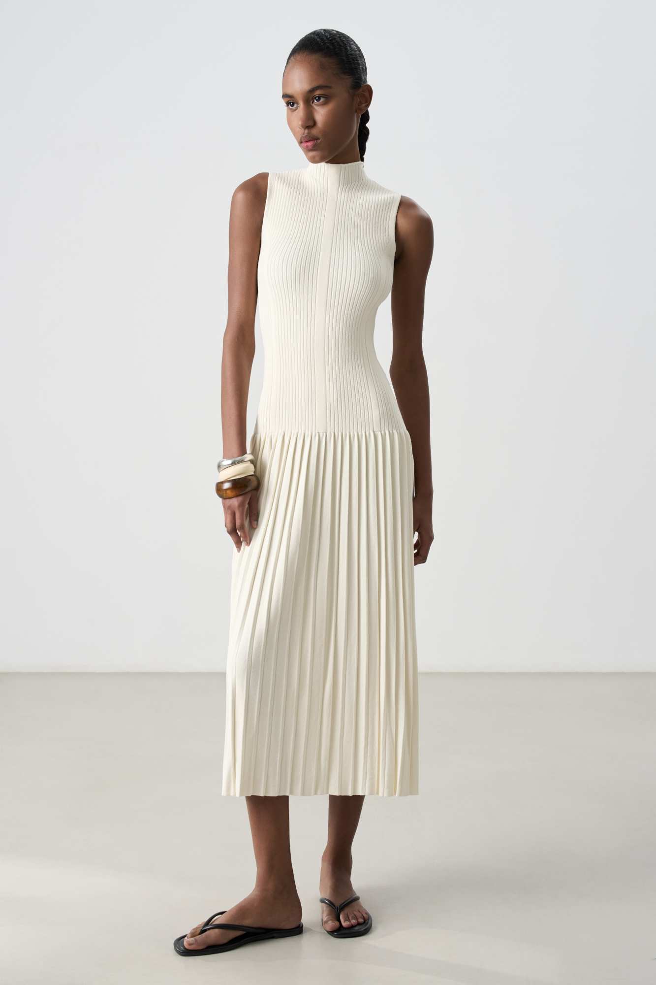Трикотажное платье длины макси из вискозы. Модель приталенного силуэта, без рукавов, с невысоким воротником-стойкой и юбкой плиссе от бедер.