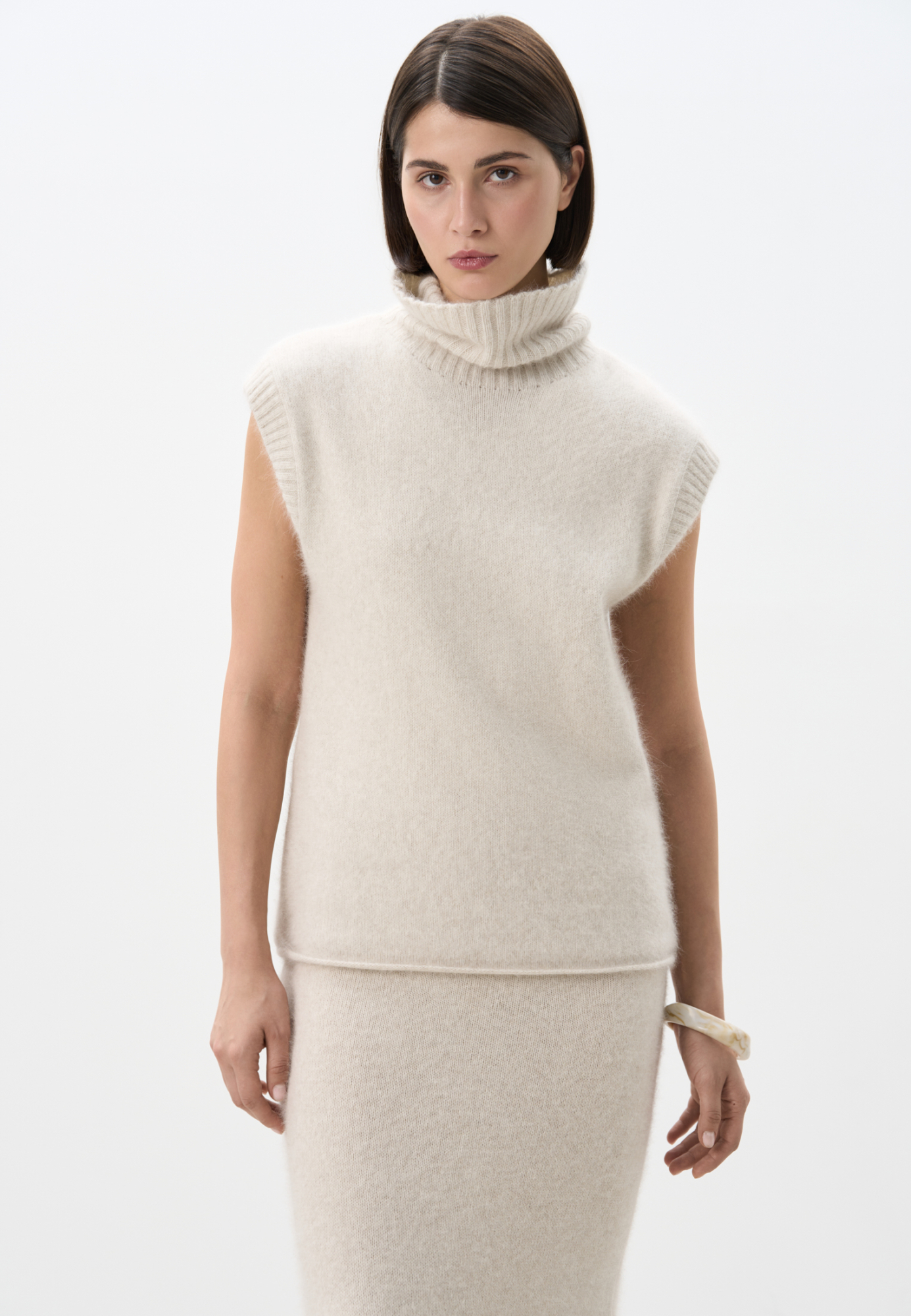 Трикотажный жилет с высоким воротом. Содержание в пряже 40% натурального пуха лисы делает жилет теплым и в тоже время очень легким. Дополнить образ можно юбкой в таком же стиле.