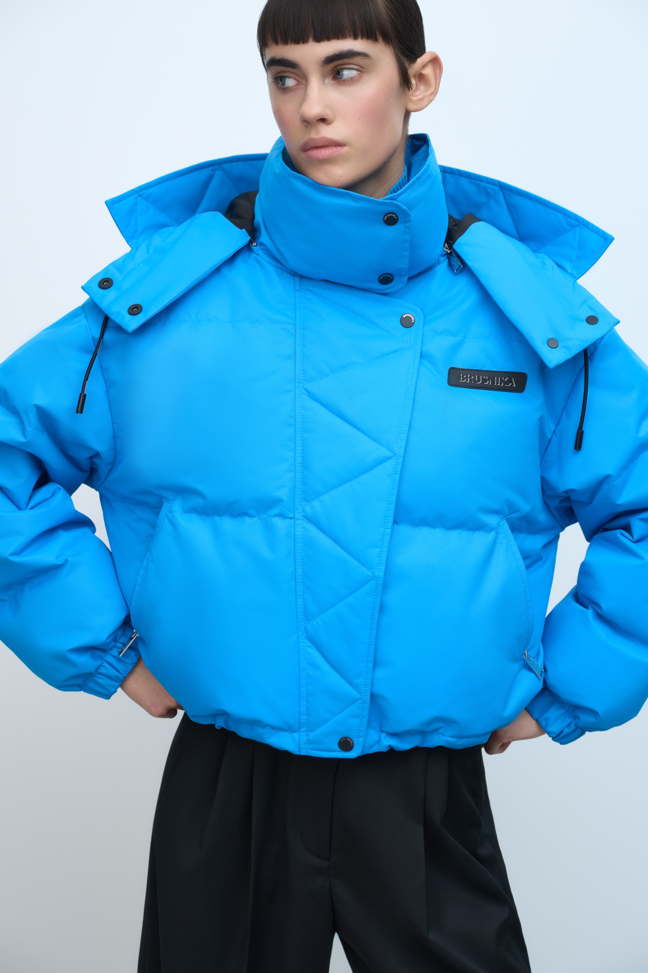 Короткий пуховик с воротником-стойкой и капюшоном на молнии. Модель свободного силуэта с боковыми карманами, спущенным плечом и брендированным ярлыком на груди. Застежка на потайную молнию и кнопки. Наполнитель натуральный пух 90% перо 10%.