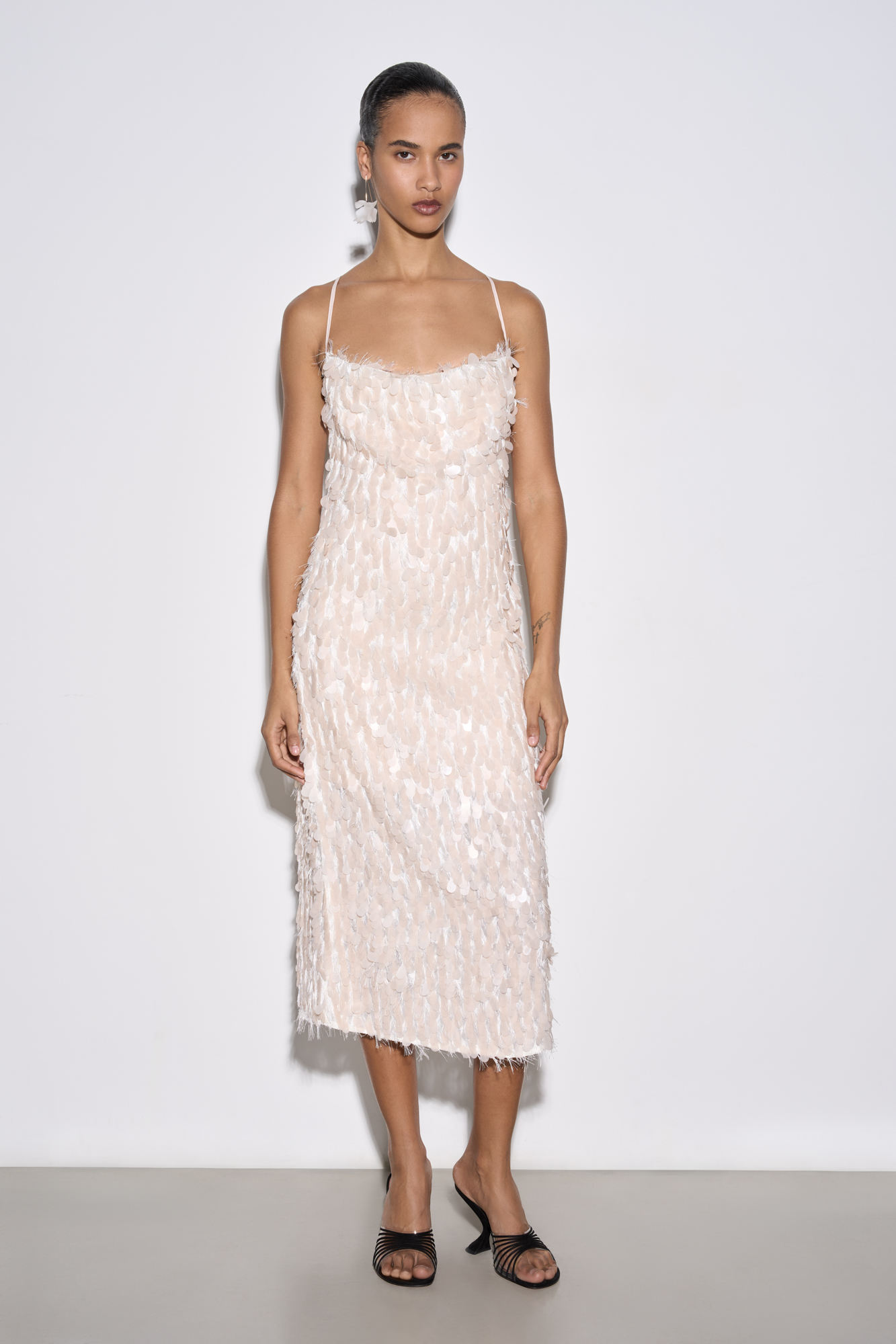 Вечернее платье-футляр длины миди, декорированное пайетками и бахромой. Модель по фигуре на тонких регулируемых бретельках. 