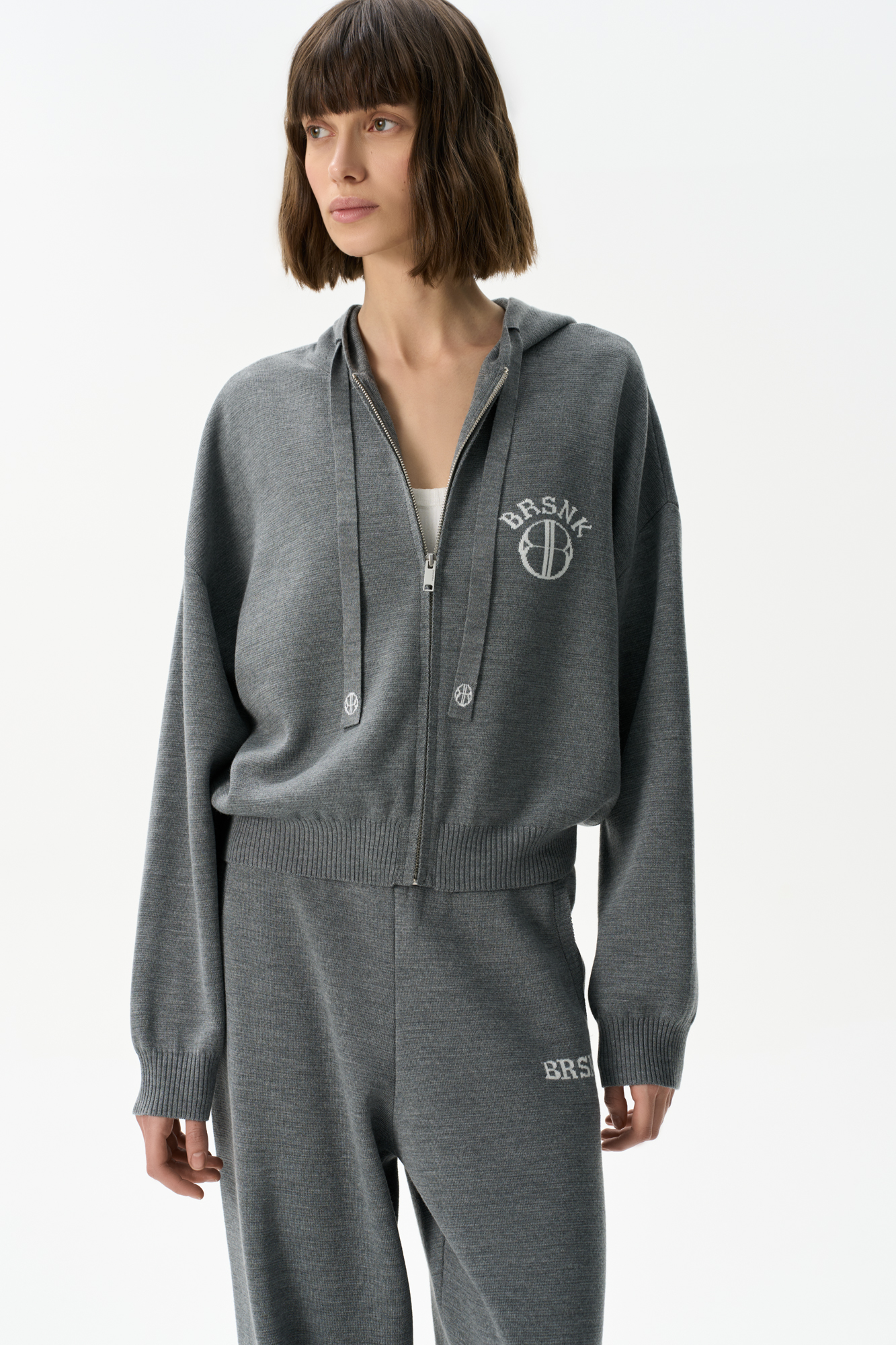 Трикотажный бомбер в спортивном стиле из шерсти с добавлением акрила. Модель свободного силуэта со спущенной линией плеча и капюшоном на кулиске. Низ изделия и манжеты рукавов выполнены на эластичной резинке. Изделие декорировано брендированным жаккардом на груди и шнурке. Застежка на молнию.