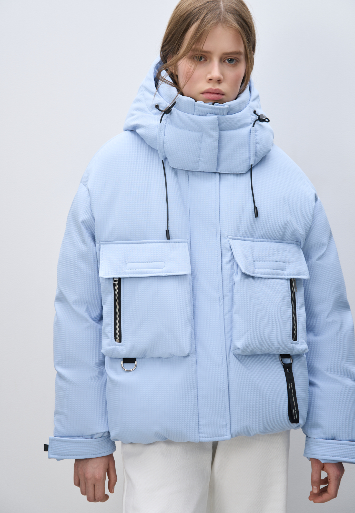 Пуховик с двумя нагрудными накладными карманами, воротником-стойкой и капюшоном. Застежка на молнию под планкой. Манжеты рукавов фиксируются липучкой. Низ изделия выполнен на регулируемой кулиске. 