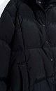 Длинный стеганый пуховик с капюшоном на кулиске. Модель свободного силуэта с воротником-стойкой, трикотажными манжетами и боковыми карманами. Застежка на молнию под планкой с брендированными пуговицами.