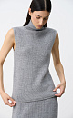 Трикотажный жилет из шерсти с добавлением акрила. Модель прямого силуэта, без рукавов, с декоративными сбавками на груди и высоким воротником с валиком. Дополнить образ можно юбкой в таком же стиле.