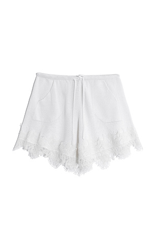 белый Трикотажные короткие шорты из 100% льна. Модель свободного силуэта с двумя карманами и поясом на кулиске. Низ изделия декорирован кружевом.