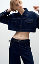 Укороченная куртка прямого кроя из денима с отложным воротником и хлястиками на поясе. Модель декорирована накладными карманами на груди, металлической фурнитурой в виде пирсинга на манжетах и брендированным ярлыком на спине. Застежка на пуговицы. 