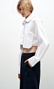 Рубашка из хлопка с добавлением полиэстера. Модель укороченного силуэта, с классическим отложным воротником, длинными рукавами и двумя накладными карманами на груди. Застежка на пуговицы. Имитация необработанного края.